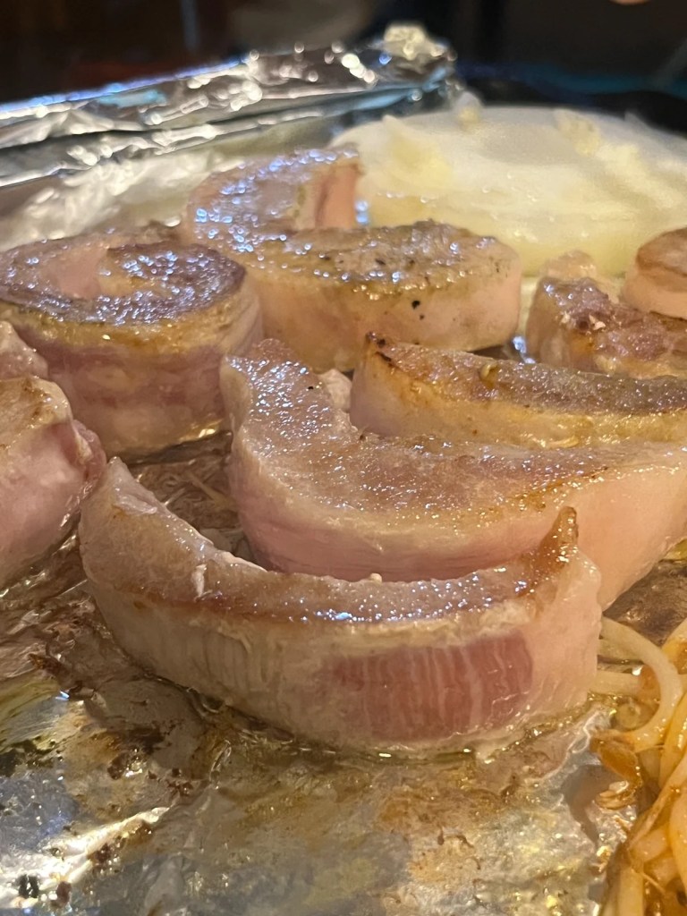Thick slices of Hwangji-sal, a premium pork cut, sizzling on a foil-lined Korean BBQ grill at Sangroksu. The rich marbling and golden-brown sear enhance the smoky, juicy flavors of this rare specialty meat.