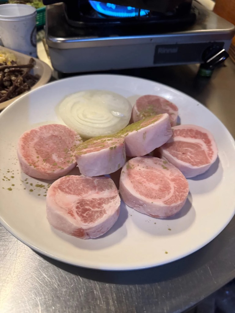 A plate of raw Hwangji-sal, a rare Korean pork cut similar to pork jowl but sliced into thick, round pieces. Served with sliced onions, this specialty cut is known for its juicy and tender texture.