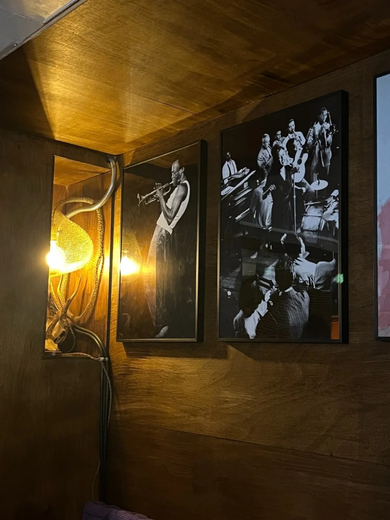 A cozy corner of Guden Guden Cafe in Yongsan, Seoul, featuring framed posters of jazz legends like Louis Armstrong and live jazz performances. The cafe plays curated jazz music, creating a warm and nostalgic ambiance for visitors.