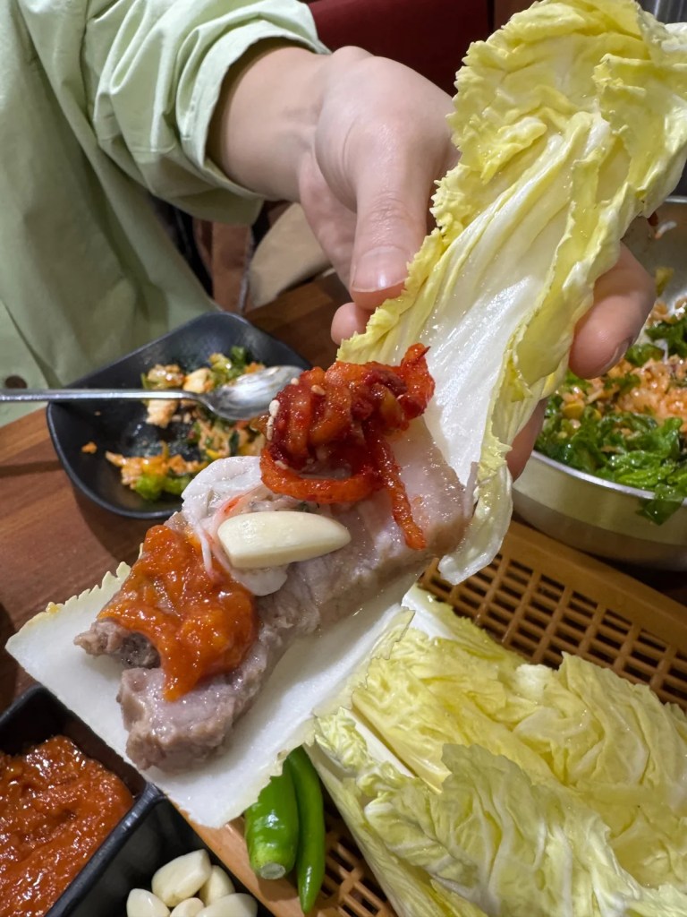 Korean cabbage wrap with pork belly, garlic, and kimchi toppings
