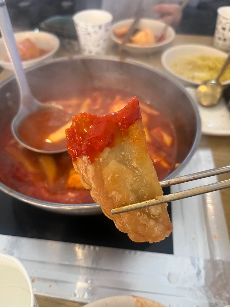 Crispy Korean twigim being dipped into a rich, spicy tteokbokki sauce for extra flavor